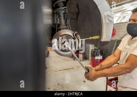 Un mécanicien latino-américain change le système de freinage d'une voiture dans un atelier Banque D'Images