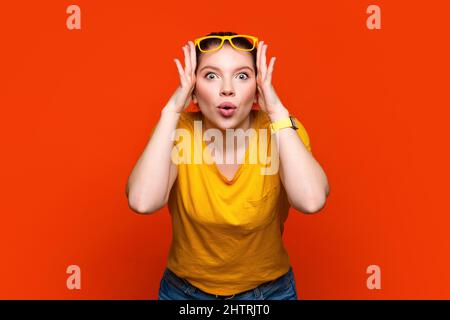 Curieuse et intriguée fille dans lumineux décontracté jaune vêtements et lunettes regardant l'appareil photo. Drôle fou comique jeune femme rend choqué grimace. Émotions de concept, expression faciale. Banque D'Images