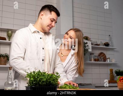 Bon couple à la maison. Concept d'alimentation saine. Beau homme et jeune femme attrayante faisant des légumes frais salade. Banque D'Images