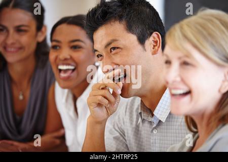 Partager la blague. Prise de vue d'un homme asiatique qui rit à une table avec ses collègues hors du foyer. Banque D'Images