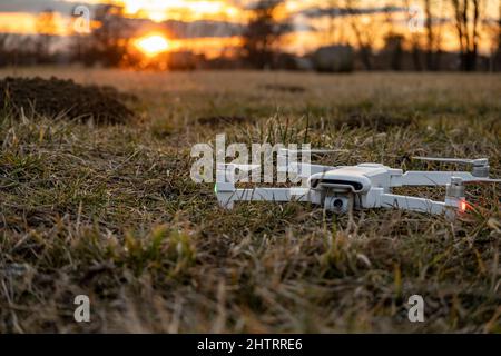 Drone blanc couché dans l'herbe sur la prairie pendant le coucher du soleil, prêt à partir Banque D'Images