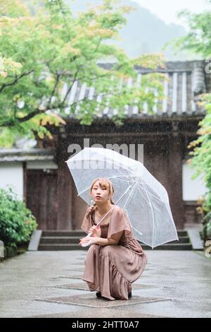 Une fille japonaise s'accroupir au sol sous un parapluie sous la pluie Banque D'Images