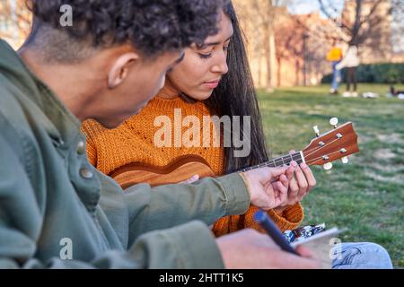 jeune musicien enseignant à une belle femme latine aux cheveux longs de jouer l'ukulele. Banque D'Images