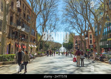 Des touristes inconnus et des habitants de la région descendent une rue piétonne à Palma Mallorca par une journée ensoleillée. Des boutiques, des arbres bordent la rue avec une fontaine à la fa Banque D'Images