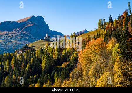 Maisons et église du village de Colle Santa Lucia, entourée de larches colorées et de pins en automne, Dolomites montagnes au loin. Banque D'Images