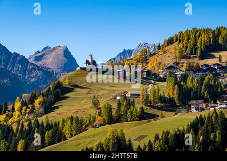 Maisons et église du village de Colle Santa Lucia, entourée de larches colorées et de pins en automne, Dolomites montagnes au loin. Banque D'Images