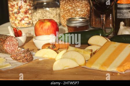 Salami au poivre sur plateau avec fromage anglais et irlandais, pommes en tranches et épices dans une cuisine rustique avec fenêtre de la cuisine Banque D'Images