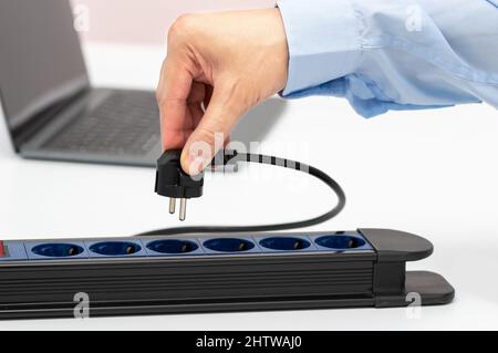 Gros plan d'un homme d'affaires de la main de brancher la fiche électrique a dans une prise sur une table Banque D'Images