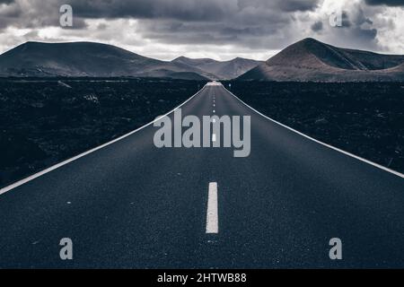 Route sans fin sur un volcan dans le parc national de Timanfaya à Lanzarote dans les îles Canaries avec une ligne continue, roches volcaniques noires sur le côté et Banque D'Images