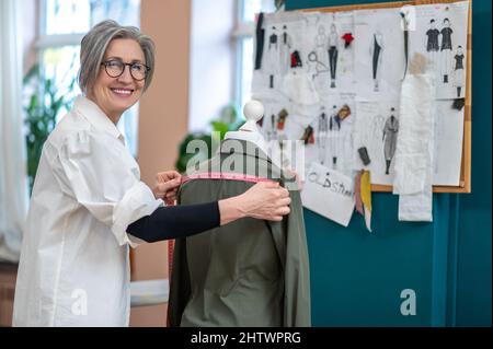 Femme souriant à l'appareil photo mettant la mesure sur le chemisier Banque D'Images