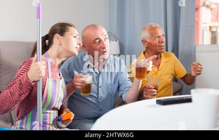 Femme assise pendant le nettoyage de la maison, mari et père regardant la télévision Banque D'Images