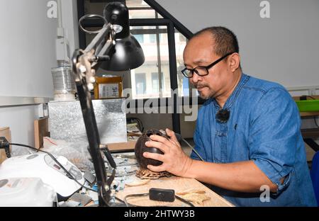 Haikou, province chinoise de Hainan. 18th févr. 2022. Zhang bidi se porte sur une coquille de noix de coco dans son studio à Qionghai, province de Hainan, dans le sud de la Chine, 18 février 2022. POUR ALLER AVEC: À travers la Chine: Les sculptures de noix de coco façonnent la vie prospère des villageois crédit: Yang Guanyu/Xinhua/Alamy Live News Banque D'Images