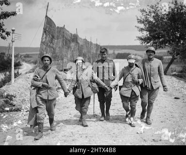 Un groupe de quatre soldats français blessés à pied. Trois des soldats français tiennent la main, guidant l'homme central qui semble avoir été blessé par le gaz : ses yeux sont couverts d'un bandage. Un soldat britannique peut être vu au centre de la photo. Banque D'Images