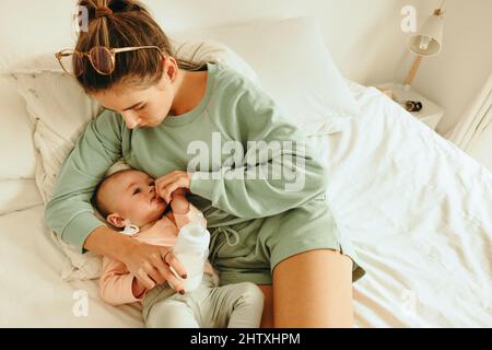 Mère allaitant son nouveau-né à la maison. Vue en grand angle d'une nouvelle maman tenant une bouteille de lait maternel tout en étant allongé à côté de son bébé sur le lit. Simple Banque D'Images