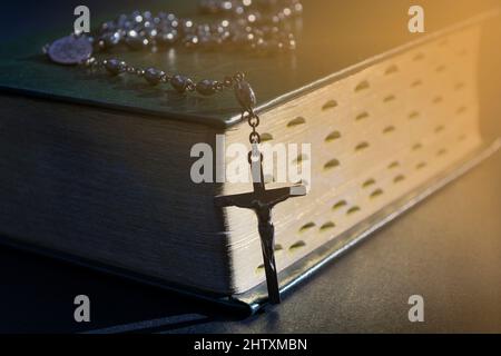 La croix sur la bible sur une table en bois avec lumière de fenêtre, ton vintage et fond sombre. Concept de religion. Banque D'Images