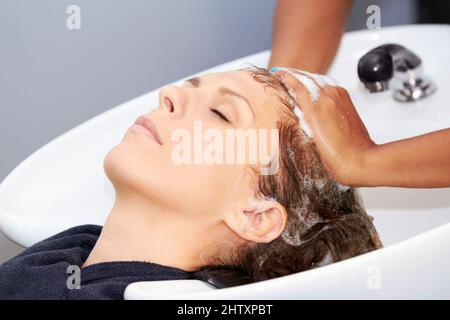 J'adore me laver les cheveux. Une jeune femme attirante se lavant les cheveux au coiffeur. Banque D'Images