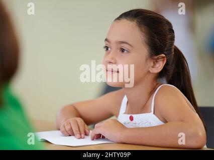 Qui aime un test. Une jeune fille enthousiaste assise à son bureau. Banque D'Images