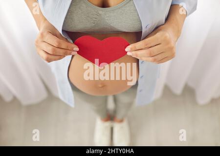 Vue de dessus de la femme enceinte tenir le coeur de papier sur le ventre Banque D'Images