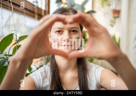 La jeune fille russo-ukrainienne, avec le drapeau de l'Ukraine et de la Russie sur son visage, montre le cœur à la main. Le concept de participation de l'ukrainien Banque D'Images