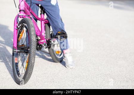 Anonyme jeune enfant d'âge scolaire élémentaire, fille assise sur un vélo, jambes de près, vue de face, arrière-plan de l'espace de copie. Enfant assis sur un vélo, signifie Banque D'Images