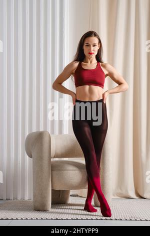 Belle femme debout avec des jambes croisées près du fauteuil dans des collants colorés Banque D'Images