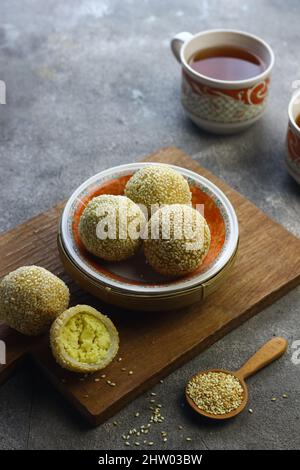 Onde de de onde ou gâteau de riz gluant boule de sésame sur plaque de céramique avec tasses de thé. Mise au point sélective, fond gris granuleux. Banque D'Images