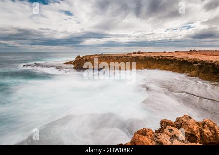 Longue exposition avec un couple touristique sur le front de la falaise avec des eaux rugueuses sur la côte sauvage de l'océan Indien à la gare de Quobba en Australie occidentale. Banque D'Images