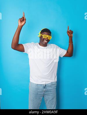 Un homme afro-américain danse avec son casque jaune et ses lunettes élégantes sur un fond bleu isolé Banque D'Images