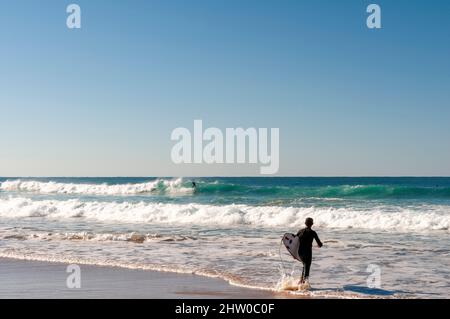 Surfeur entrant dans l'eau avec leur planche sur la belle plage portugaise Banque D'Images