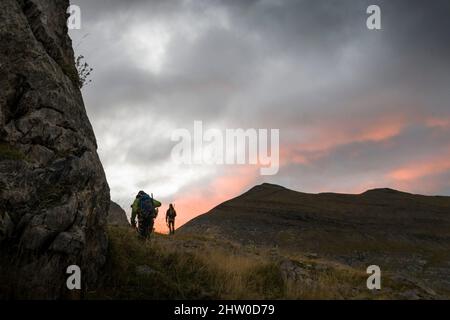 Randonneurs montant en contre-jour au lever du soleil sous les nuages Banque D'Images