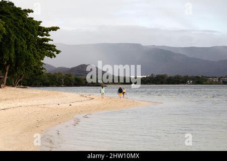 Personnes marchant sur la plage de Flic en Flac à l'île Maurice. Les filao et les palmiers poussent sur la plage avec est lappé par l'eau de l'océan Indien. Banque D'Images