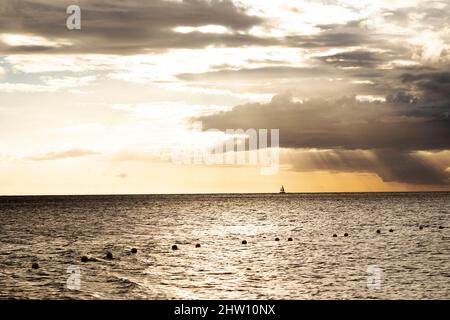 Un yacht navigue dans la baie de Tamarin, au large de la côte sud-ouest de l'île Maurice. Les nuages de pluie pendent dans le ciel autrement doré au-dessus de l'océan Indien. Banque D'Images