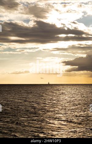 Un yacht navigue dans la baie de Tamarin, au large de la côte sud-ouest de l'île Maurice. Les nuages de pluie pendent dans le ciel autrement doré au-dessus de l'océan Indien. Banque D'Images