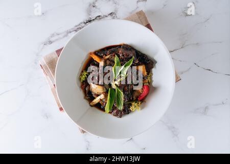 Bœuf au poivre noir avec champignons, tomates, oignons dans un plat isolé sur le dessus du tapis vue sur fond de marbre gris Banque D'Images