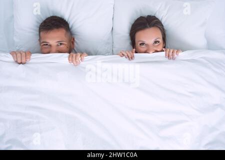 Beau couple heureux dans le lit se cachant et couvrant le visage avec une couverture blanche. Concept de relation. Copier l'espace Banque D'Images