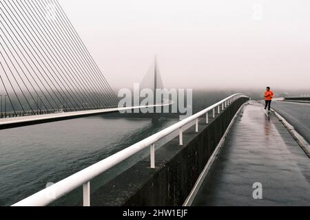 France, Finistère, Brest, homme qui court sur le pont Albert Loupe à côté du pont Iroise par temps pluvieux Banque D'Images