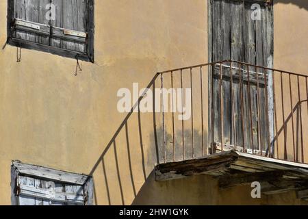 Ancienne façade de maison rurale traditionnelle avec un mur en stuc ocre, des volets en bois gris clair et une rampe d'escalier en fer forgé rouillé à Nafplio, en Grèce. Banque D'Images