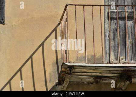 Ancienne façade de maison rurale traditionnelle avec un mur en stuc ocre, des volets en bois gris clair et une rampe d'escalier en fer forgé rouillé à Nafplio, en Grèce. Banque D'Images