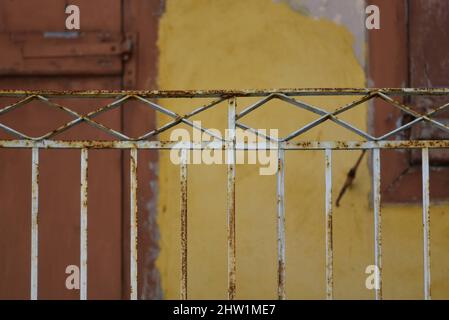 Ancienne façade de maison rurale avec un mur en stuc ocre, des volets de fenêtre en bois brun et une balustrade de balcon en fer forgé aux intempéries rouillées à Nauplie, en Grèce. Banque D'Images