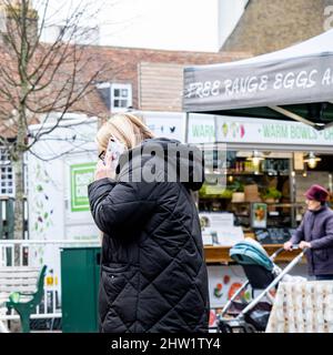 Epsom Surrey Londres, Royaume-Uni, mars 03 2022, une femme debout seule utilisant Un téléphone mobile sur Une place du marché Banque D'Images