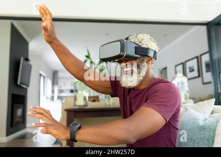 Un homme senior afro-américain heureux danse tout en regardant le simulateur de réalité virtuelle à la maison Banque D'Images