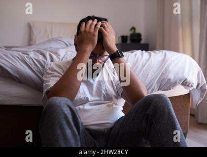 Un homme adulte s'assoit à l'extrémité de son lit avec sa tête dans les mains, déprimé. Banque D'Images