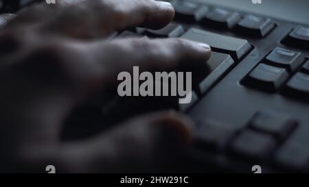 Gros plan, un homme appuie sur la touche du clavier.L'homme appuie sur le bouton pour entrer dans le clavier de l'ordinateur.La main de l'homme appuie sur le clavier à la lumière de l'écran de l'ordinateur. Banque D'Images