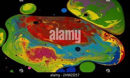 Surface avec des taches d'encre acrylique de couleur rouge, verte, bleue, rose et jaune. Gros plan de peintures liquides mélangées isolées sur fond noir. Banque D'Images