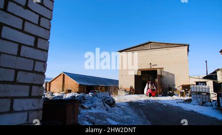 Chariot élévateur sur site de production. Films. Un petit chariot élévateur conduit sur le site de production de l'usine en arrière-plan d'un grand entrepôt en hiver Banque D'Images