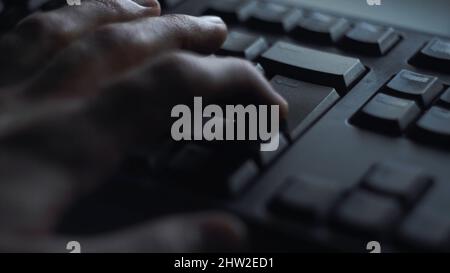 Gros plan, un homme appuie sur la touche du clavier.L'homme appuie sur le bouton pour entrer dans le clavier de l'ordinateur.La main de l'homme appuie sur le clavier à la lumière de l'écran de l'ordinateur. Banque D'Images