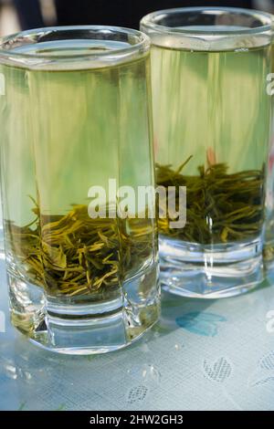 Infusion fraîchement faite de thé de Chine; eau bouillante versée d'une théière d'eau chaude dans des feuilles de thé chinois coupées épaisses dans des verres de verre. Ville de Songpan dans le nord du Sichuan, en Chine. (125) Banque D'Images