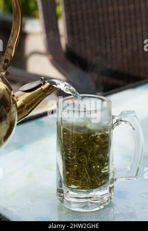 Infusion fraîchement faite de thé de Chine avec de l'eau bouillante versée d'une théière d'eau chaude dans des feuilles de thé chinois coupées épaisses dans des verres en verre. Ville de Songpan dans le nord du Sichuan, en Chine. (125) Banque D'Images