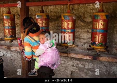 Mère et bébé, peuple bouddhiste local du Tibet et de l'utilisation du patrimoine tibétain / tourner les roues de prière / tourner une roue pour prier. Langmusi, Chine. Langmusi est au bord du plateau tibétain. (125) Banque D'Images