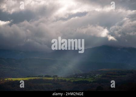 Un rayon de soleil se brise à travers les nuages et illumine quelques prairies entre les montagnes de Cervantes Ancares en Galice Banque D'Images